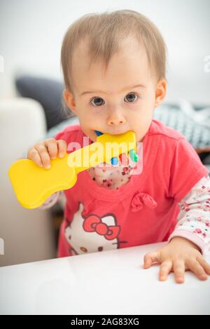 Caucasien mignon bébé de 1 an fille jouet guitare jaune morsures, concept de jouets de dentition, les morsures de l'enfant. Fille en chemise rouge hello kitty Banque D'Images