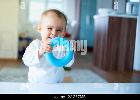 Caucasian baby girl standing next to table avec tore bleu dans les mains et rire Banque D'Images