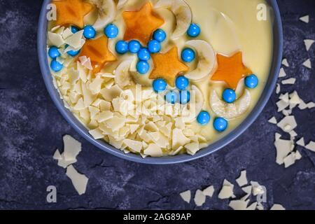 Vue de dessus du bol rempli de fruits et de yogourt décoré avec des morceaux de smoothie banane et persimmon en forme d'étoiles et de lunes, garni de c blanc Banque D'Images