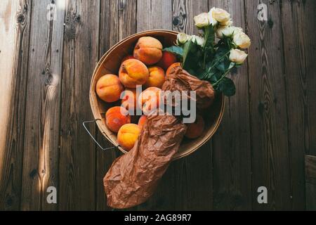 Photo grand angle d'un bol avec des pêches et un bouquet de roses blanches Banque D'Images