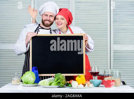 Couple in love cuisiner ensemble. Les valeurs familiales. Partager la joie. L'homme et la femme chef cooking aliments ensemble. Couple avec tableau noir pour fins de publicité. Belle famille à la cuisine. Restaurant familial. La fête de la famille. Banque D'Images