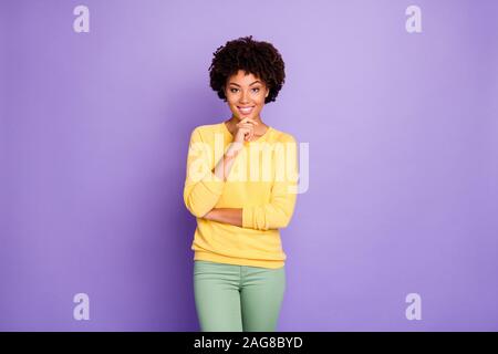 Photo de cheerful perplexe jolie fille portant des vêtements jaune devant la caméra de toucher son menton smiling toothily transmission isolated over purple Banque D'Images