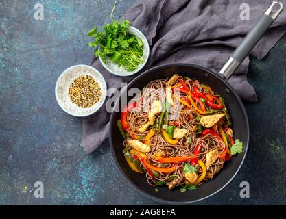 Nouilles soba sarrasin plat japonais avec le poulet et les légumes la carotte, le poivron et les haricots verts dans le wok sur fond bleu foncé Banque D'Images