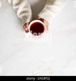 Woman holding tasse de thé chaud sur la table de marbre beige pierre, photo gros plan des mains de pull-over chaud avec une tasse, un matin d'hiver, concept vue supérieure Banque D'Images
