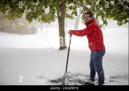 Homme portant une veste rouge prenant un repos de pelletage neige avec un arrière-plan flou Banque D'Images