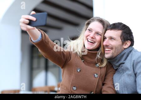Heureux couple d'adultes prenant autoportraits avec un téléphone mobile en hiver dans la rue Banque D'Images