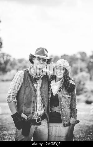 Photo verticale en niveaux de gris d'un couple portant une tenue de cow-boy tout en souriant à l'appareil photo Banque D'Images