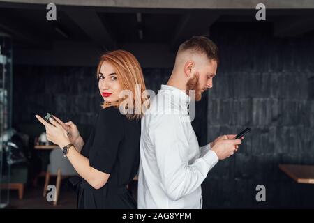 Les jeunes se tenir avec le dos à l'autre avec un smartphones dans les mains. Banque D'Images