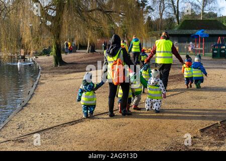 Un groupe d'enfants d'une école maternelle dans une haute visibilité vestes marcher avec les enseignants ou l'enfance dans un parc en hiver Banque D'Images