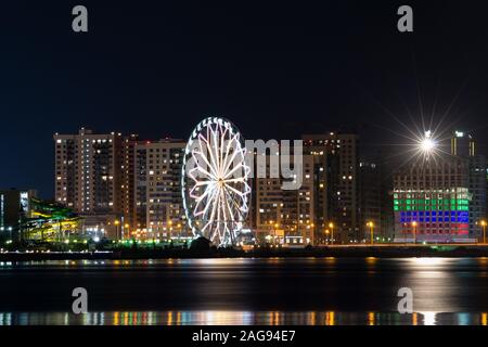 Paysage urbain avec une grande roue et beaucoup d'illuminé bâtiments reflétés dans le lac la nuit Banque D'Images