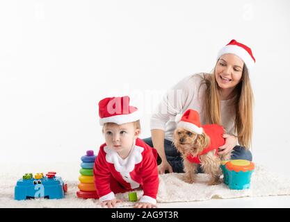 Stock studio photo de bébé déguisé en Père Noël sur le sol accompagné de sa mère et un chien et sont roulées avec des jouets Banque D'Images