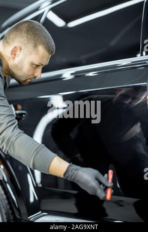 L'examen des travailleurs caisse pour les rayures et les dommages par backliting qu'une lampe de poche, le service. Contrôle de la peinture avant de voiture véhicule Banque D'Images