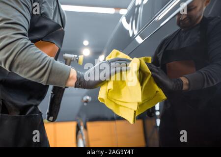 Service de location de véhicule avec corps d'essuyage travailleur microfibre, examinant le revêtement brillant après polissage intérieur. Et l'entretien esthétique automobile professionnel concept Banque D'Images