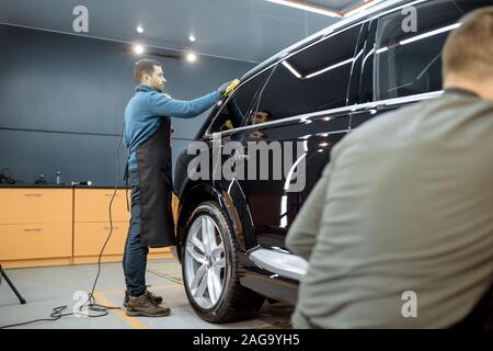 Les travailleurs des services de voiture avec caisse d'essuyage microfibre, examinant le revêtement brillant après polissage intérieur. Et l'entretien esthétique automobile professionnel concept Banque D'Images