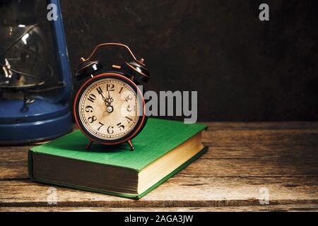 Ancienne rétro réveil en intérieur rustique avec des livres et lampe à kérosène.Close up. Banque D'Images