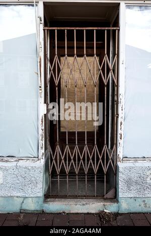 Porte d'une boutique abandonnée fixé avec une grille en acier, les fenêtres sont scellées avec du papier et feuilles Banque D'Images