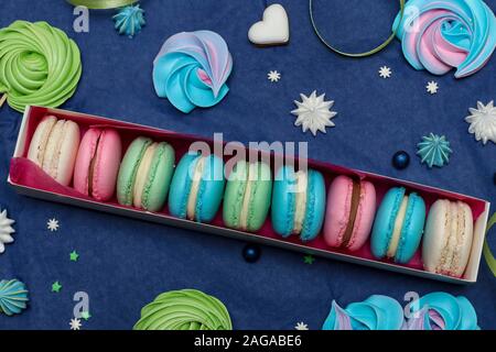 Délicieux macarons sucrés multicolores dans une boîte-cadeau blanche sur un fond bleu classique, vue du dessus Banque D'Images