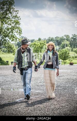 Photo verticale d'un couple portant une tenue de cow-boy et tenir les mains en marchant Banque D'Images