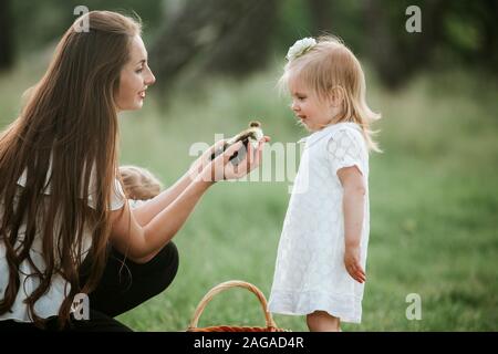 Mère montre des enfants peu de canetons dans panier d'osier. petit canard dans les mains d'une femme. La maman montre à sa fille un petit canard Banque D'Images