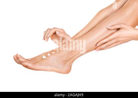 Jolie femme l'application de la crème sur ses jambes isolé sur fond blanc. Vue rapprochée d'une femme aux jambes avec la peau parfaite et les mains Banque D'Images