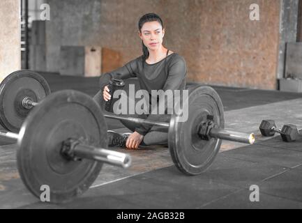Fatigué femme assise dans une salle de sport sur le sol avec des barres. Concept lyfestyle en bonne santé. Banque D'Images