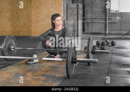 Fatigué femme assise dans une salle de sport sur le sol avec des barres. En bonne santé et sport concept lyfestyle. Banque D'Images