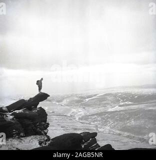 Années 1950, historique, hivernal et marcheur masculin debout sur une corniche rocheuse, en regardant le paysage environnant, Lake District, Cumbria, Angleterre, Royaume-Uni. Banque D'Images