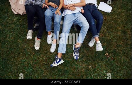 Vue de particules. Groupe de jeunes étudiants dans les tenues sur l'herbe verte dans la journée Banque D'Images