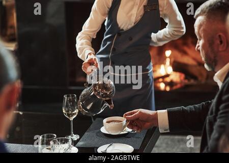 Atmosphère chaude. Female waiter pouring thé chaud dans la tasse blanche. Les amis se trouve dans le restaurant avec belle cheminée dans c Banque D'Images