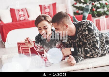 Excité comme un enfant à nouveau. Joli jeune couple couché sur le plancher de salle de séjour au moment de la nouvelle année avec les coffrets cadeaux Banque D'Images