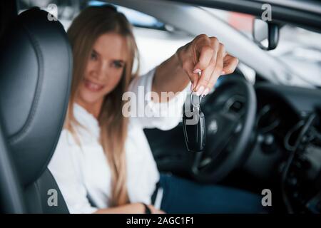 Heureux propriétaire avec des clés en main. Belle fille blonde assise dans la nouvelle voiture avec intérieur noir moderne Banque D'Images