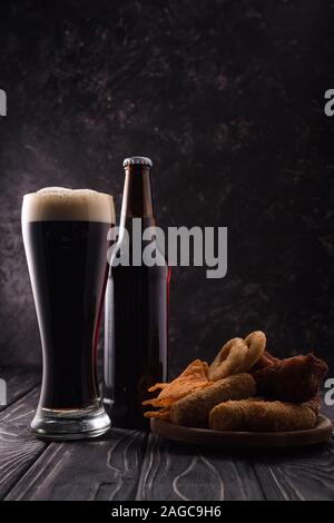 Bouteille et verre de bière près de la plaque avec des collations sur table en bois Banque D'Images