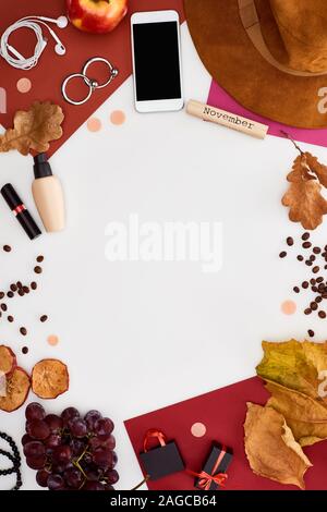 Smartphone, hat, des feuilles sèches, frais et sec, pommes, raisins, Donut, cosmétiques, les grains de café et la cale en bois avec inscription novembre isolé sur whit Banque D'Images