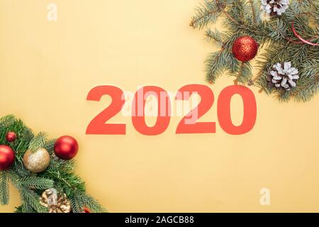 Vue de dessus les numéros 2020 papier près de branches d'arbre de Noël avec des cônes et babioles sur fond jaune Banque D'Images