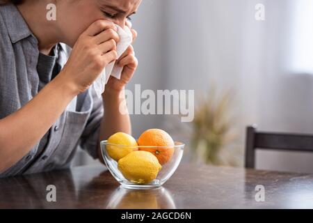 Femme aux yeux clos l'éternuement dans les tissus près d'orange et les citrons dans un bol Banque D'Images