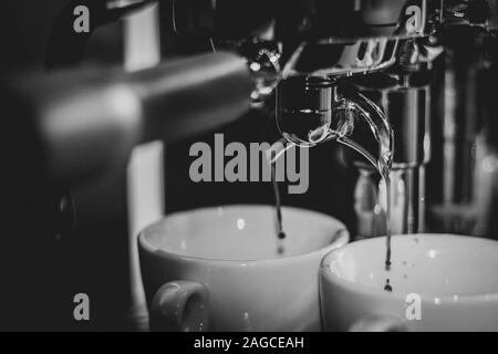 Un portrait noir et blanc de la tuyère d'une machine à café. Et du café chaud fraîchement préparé est fabriqué à partir de grains moulus. Banque D'Images