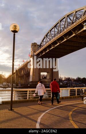 Un couple marche le long du sentier piétonnier sous le pont de la rue Burrard au coucher du soleil, à Vancouver, en Colombie-Britannique, au Canada Banque D'Images