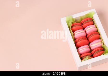 De savoureux biscuits macaron macaron sucré, dans une boîte cadeau blanche sur fond rose, rouge et rose macarons Banque D'Images