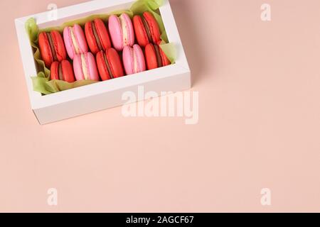 De savoureux biscuits macaron macaron sucré, dans une boîte cadeau blanche sur fond rose, rouge et rose macarons Banque D'Images