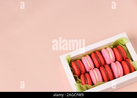 De savoureux biscuits macaron macaron sucré, dans une boîte cadeau blanche sur fond rose, rouge et rose macarons Banque D'Images