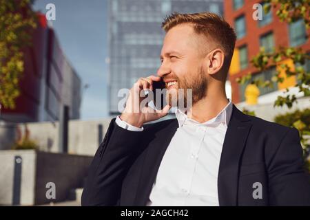 Businessman talking on the phone sur l'arrière-plan de bâtiment d'affaires. Banque D'Images