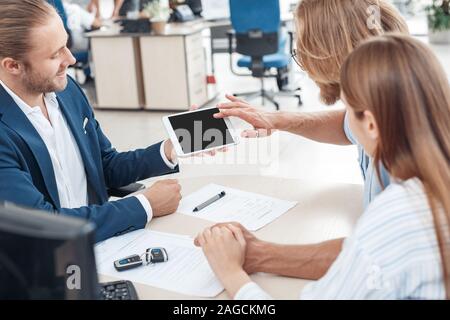 Location de Salon de coiffure. Jeune couple assis à table avec la présentation de l'agent sur voiture tablette numérique heureux tandis que les clients de toucher écran curieux Banque D'Images