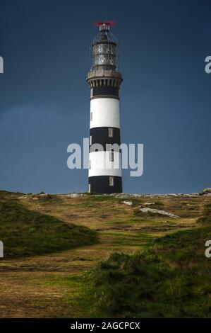 Photo verticale d'un phare sous l'obscurité ciel dans un champ herbacé Banque D'Images