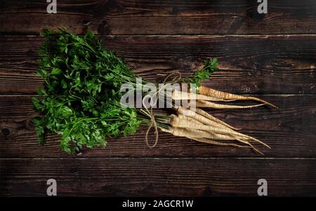Deux bouquets de persil panais, racines et feuilles vertes, à égalité avec cordon, photo prise à la verticale sur la planche de bois foncé Banque D'Images