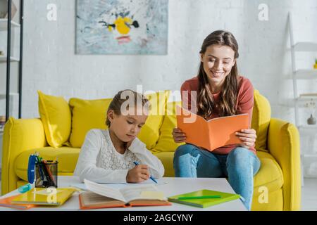 Focus sélectif de garde près de l'ordinateur portable attrayant holding mignon enfant qui étudie à la maison Banque D'Images