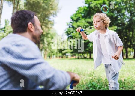 Père et fils jouant avec des bulles de savon dans park Banque D'Images