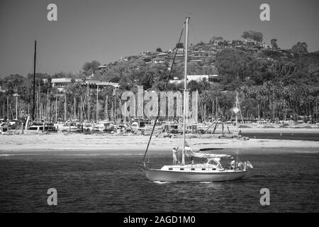 Un homme Hissez la grand voile, tandis qu'une femme dirige un voilier hors du port de Santa Barbara vers le Pacifique à Santa Barbara, CA, en noir et blanc Banque D'Images