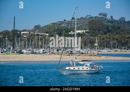 Un homme Hissez la grand voile, tandis qu'une femme dirige un voilier hors du port de Santa Barbara vers le Pacifique à Santa Barbara, CA, Banque D'Images