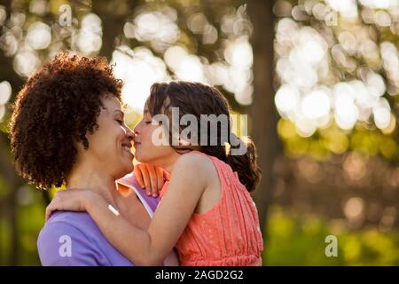 Smiling woman d'être embrassé par sa fille alors qu'elle la tient dans la forêt. Banque D'Images