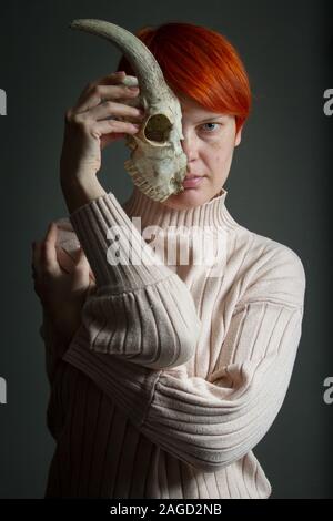 Portrait of a middle-aged woman holding rousse la moitié d'un crâne de chèvre devant son visage, duplicité concept Banque D'Images